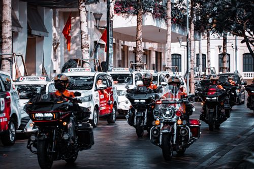 Free Motorcyclists ride through a lively city street alongside taxis, showcasing urban travel and vehicle diversity. Stock Photo