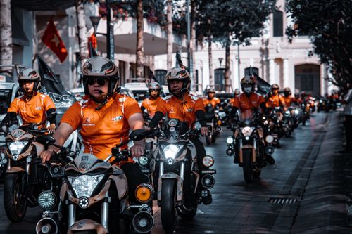 Free Group of bikers in orange riding motorcycles through a city street during the day. Stock Photo
