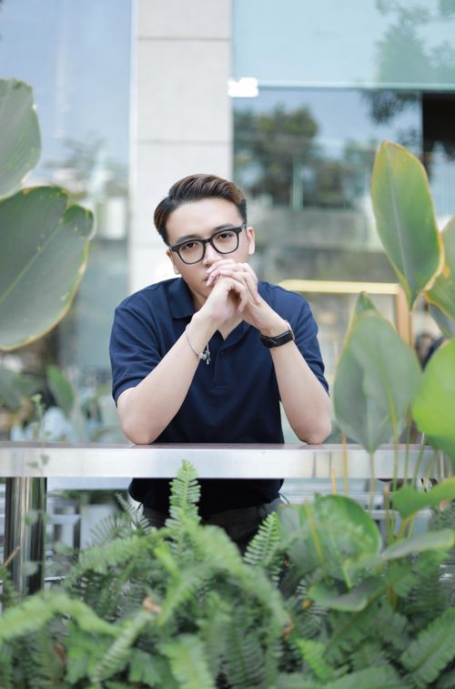 Free Stylish man in navy shirt and eyeglasses leaning on a railing surrounded by lush greenery. Stock Photo