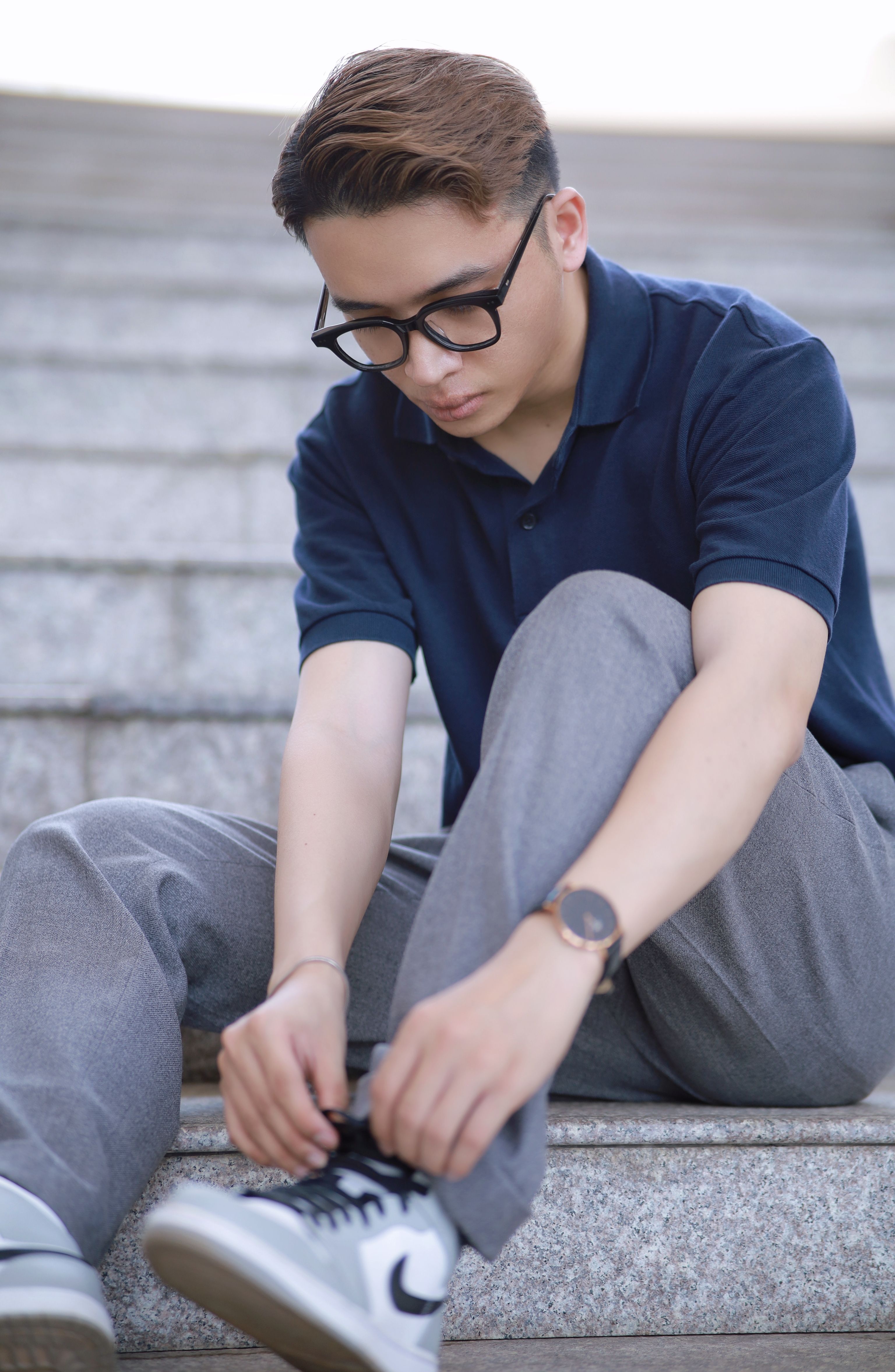 A young man in casual attire adjusting his shoes while sitting on outdoor steps.