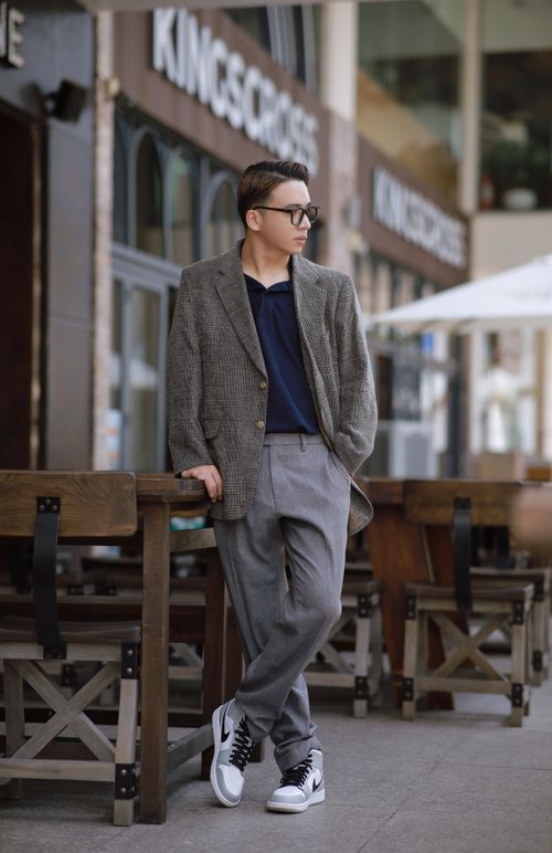 Free Man in glasses wearing a blazer and sneakers, posing stylishly in an outdoor cafe setting. Stock Photo