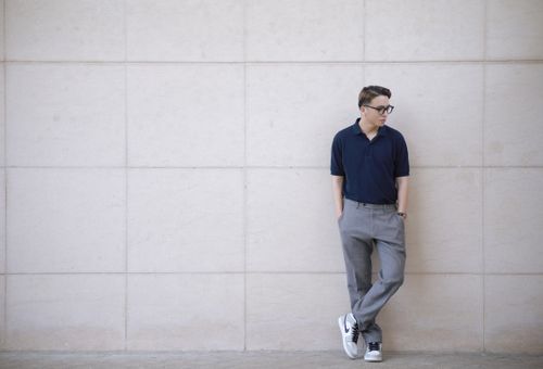 Free A fashionable man in eyeglasses poses against a minimalist wall, exuding urban style. Stock Photo
