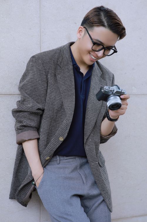 Free Fashionable young man smiling while holding a camera, wearing a jacket and eyeglasses. Stock Photo