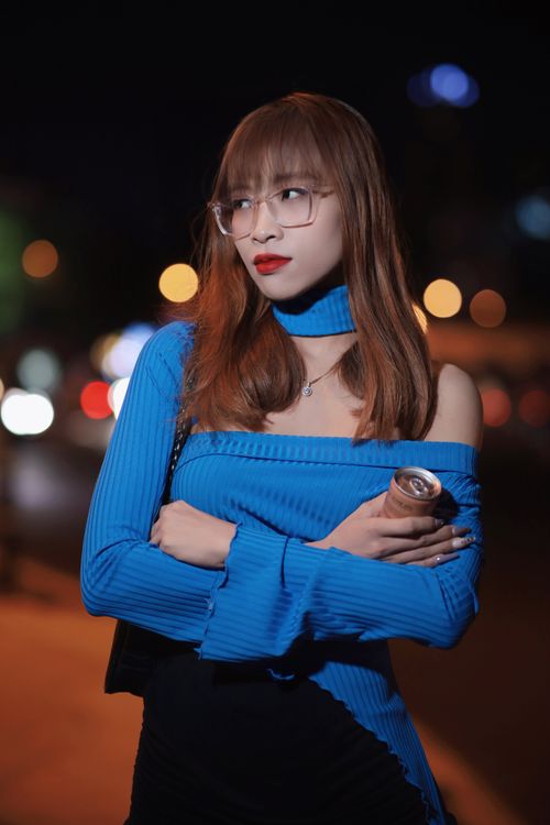 Free A fashionable woman in a blue blouse and glasses poses at night with bokeh lights. Stock Photo
