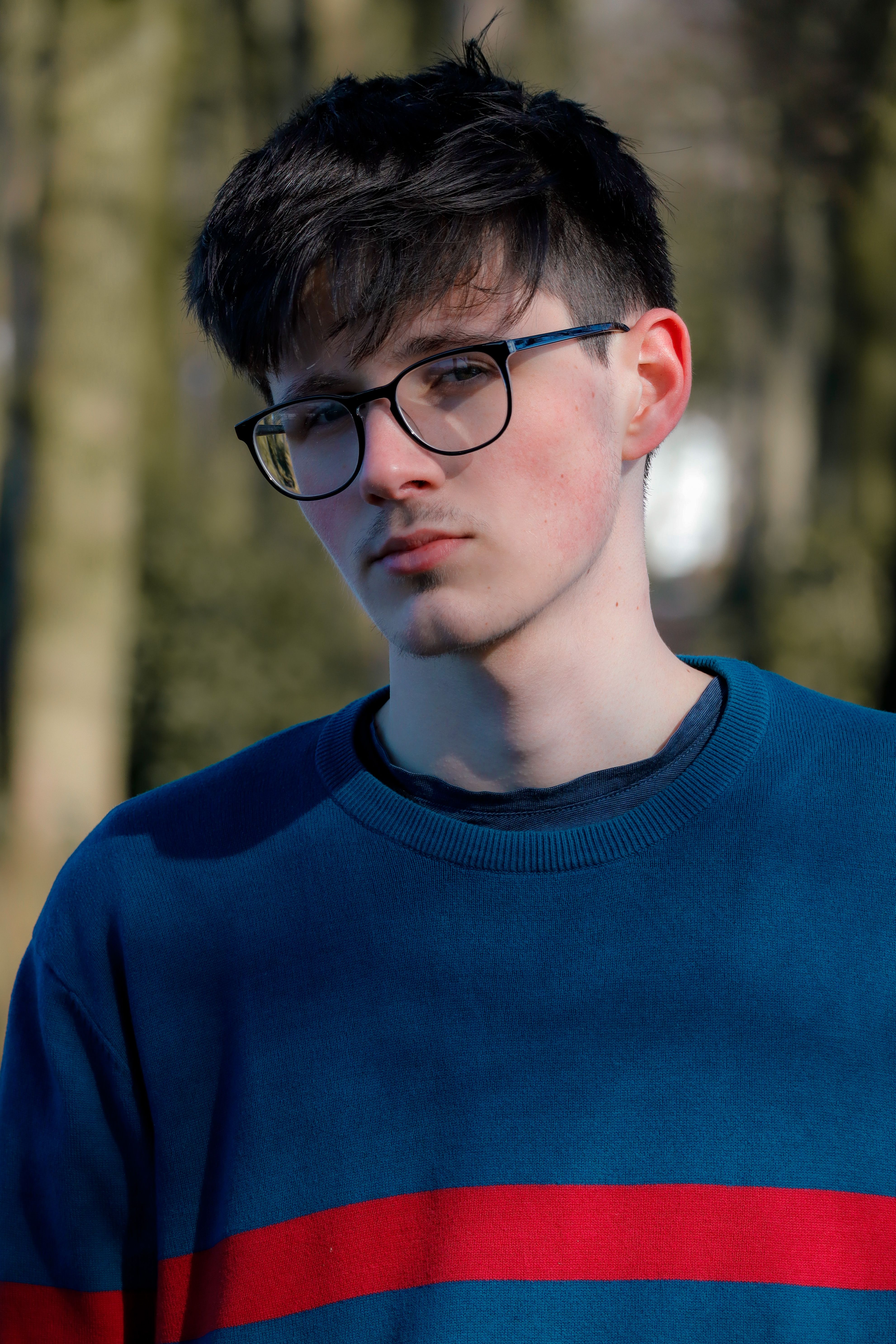 Casual portrait of a young man wearing glasses and a sweater, enjoying a sunny day outdoors.