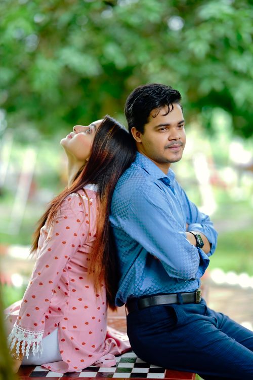 Free A couple sitting back to back on a bench in a sunny park, exuding leisure and relaxation. Stock Photo