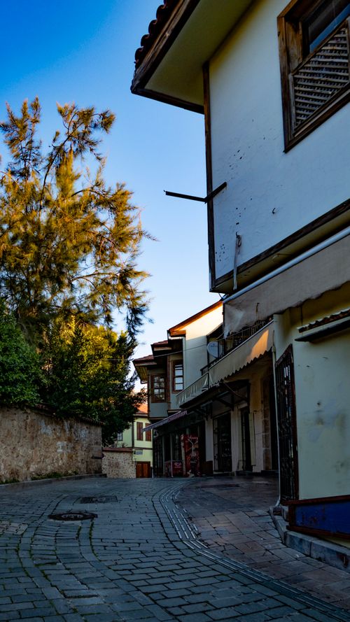 Free A picturesque narrow street with traditional architecture and lush trees on a sunny day. Stock Photo