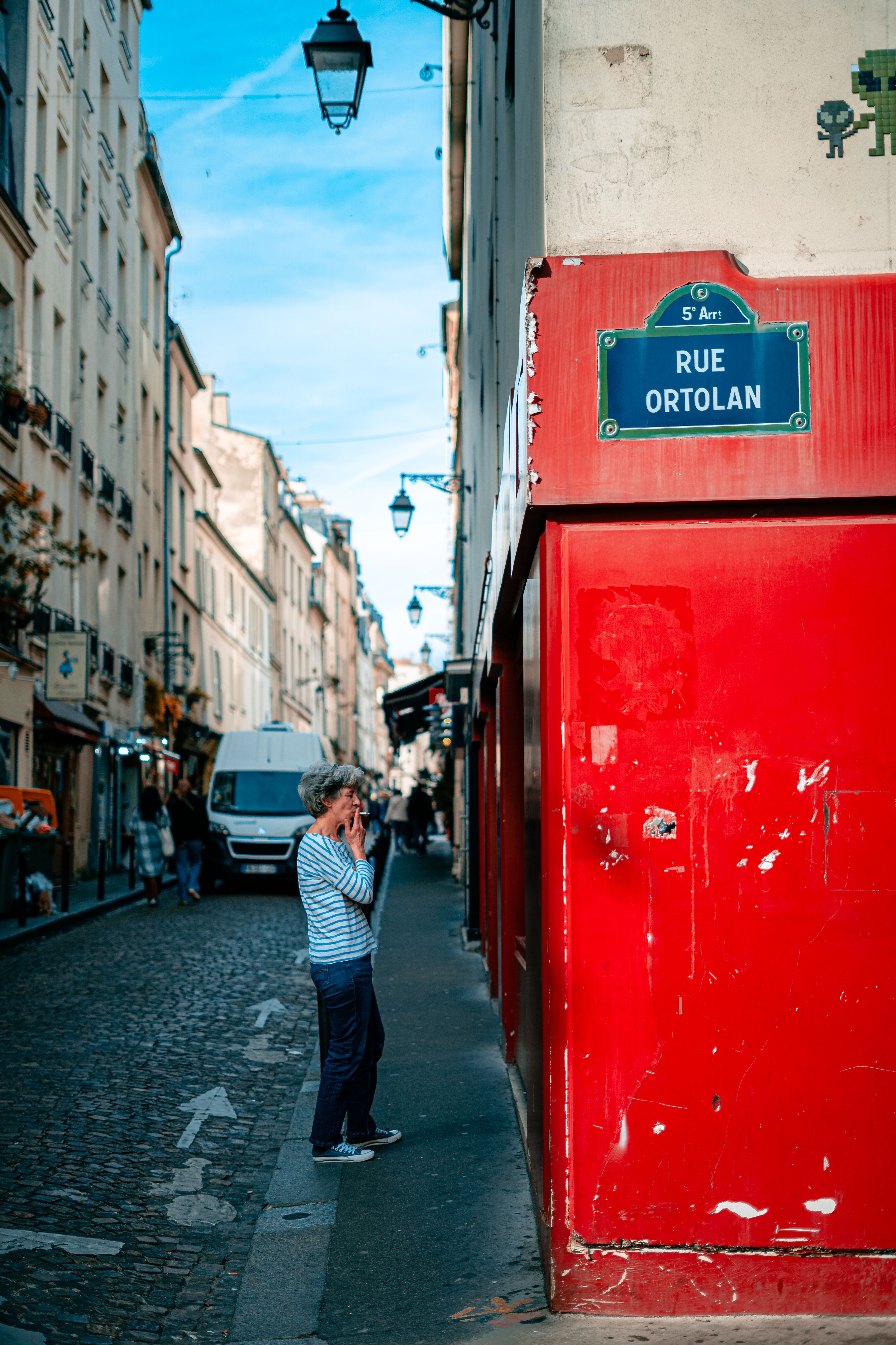 Elderly woman enjoying a sunny day on Rue Ortolan, Paris. Classic urban atmosphere.