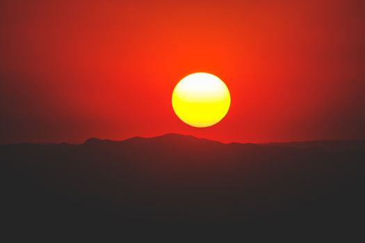 Captivating sunset with a bold sun against red sky over silhouette mountains.