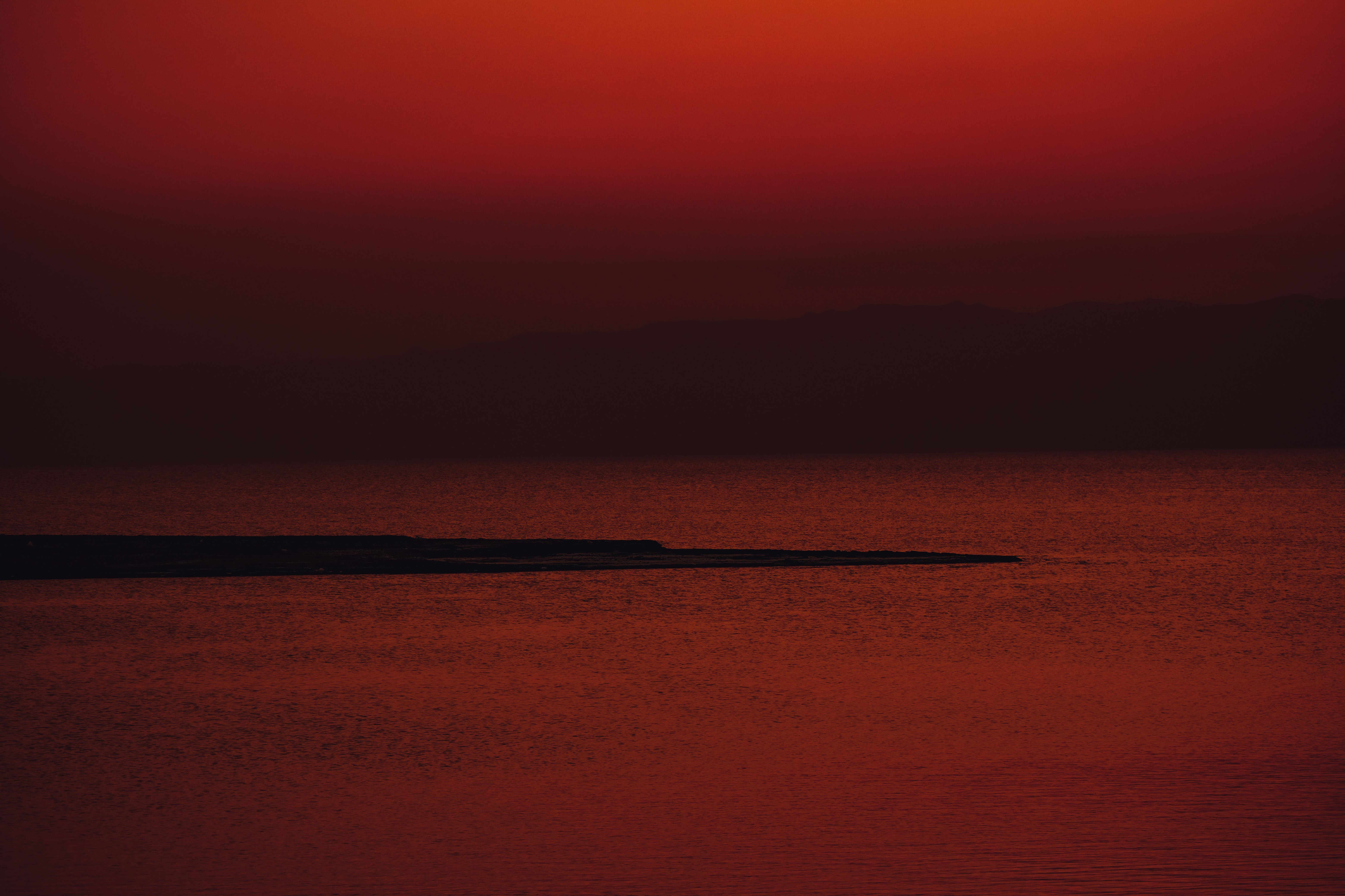 A striking red sunset creates a dramatic, tranquil seascape with a distant peninsula.