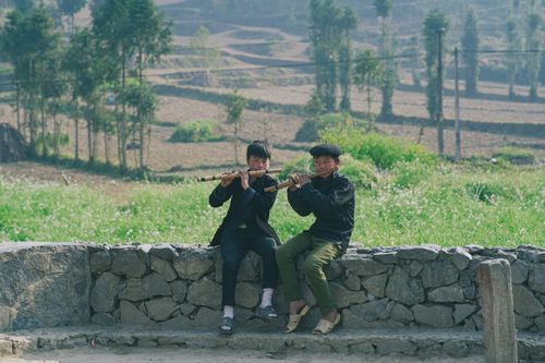 Free Two boys play flutes by a stone wall in a rural Vietnamese village, enjoying music outdoors. Stock Photo