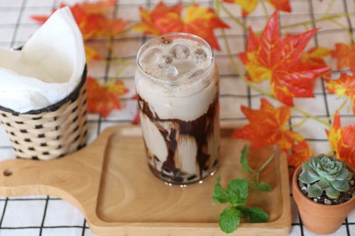 Free A refreshing iced coffee topped with chocolate syrup, surrounded by autumn leaves and decor. Stock Photo