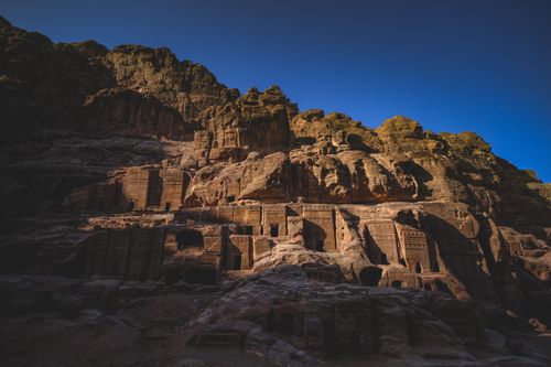 Free Historic rock-carved buildings sunlit against clear blue sky in Petra, Jordan. Stock Photo