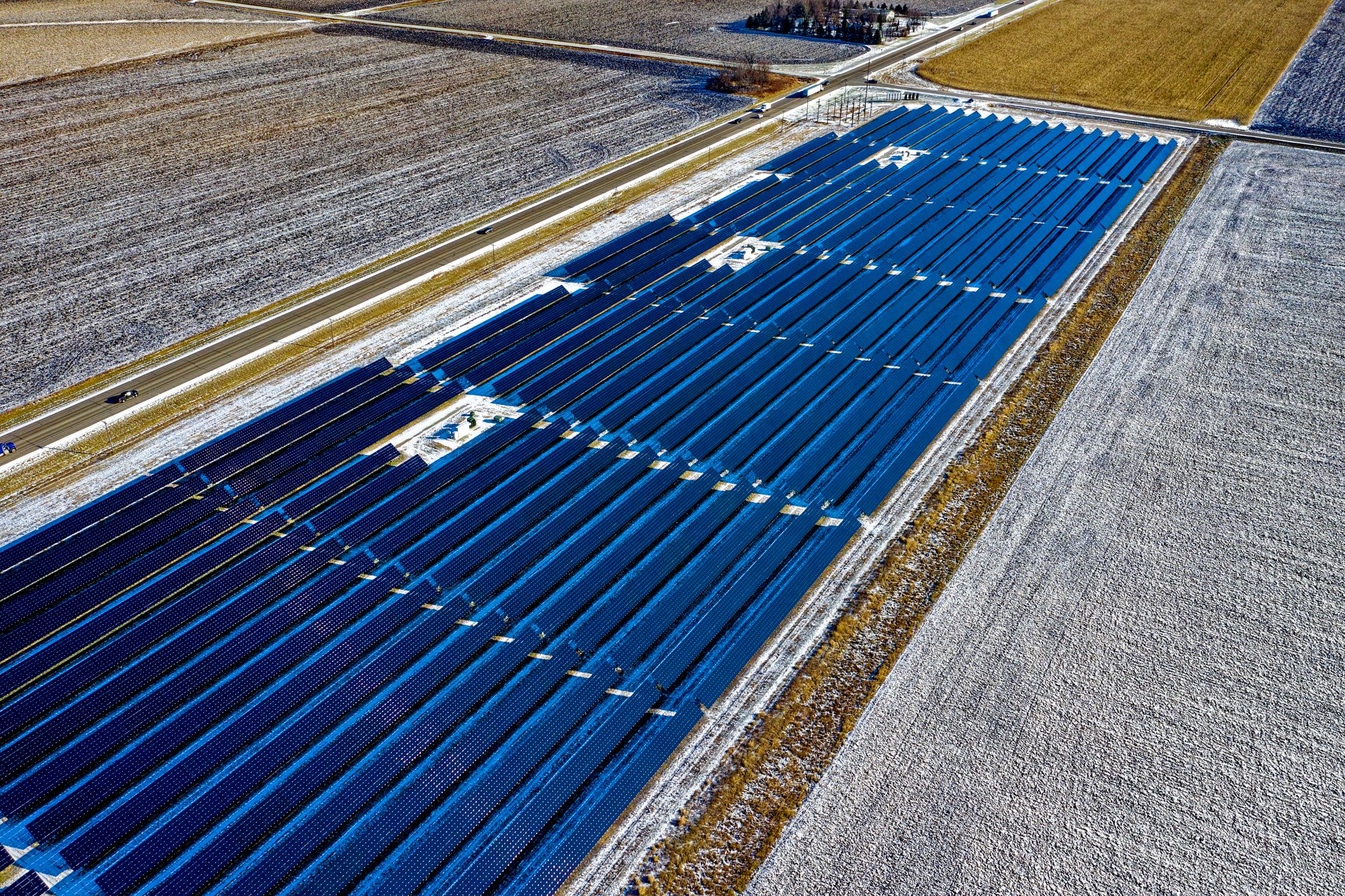 Aerial shot of expansive solar panel installation in snowy fields during daylight in Claremont, MN.
