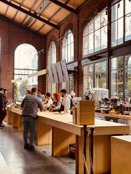 Spacious café with patrons at the counter, featuring industrial-style brick walls and arched windows.