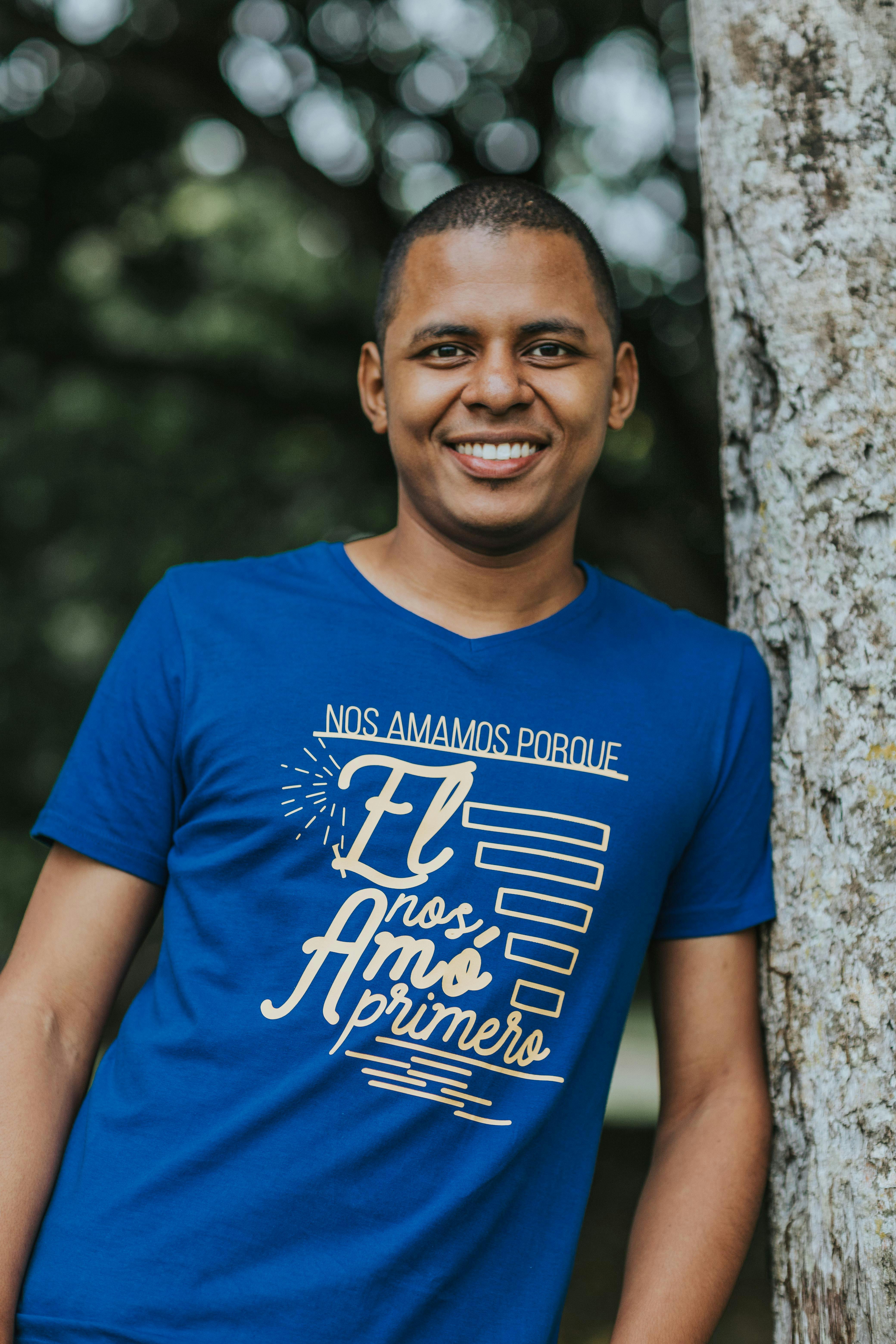 Young man smiling by a tree with a positive message on his shirt.