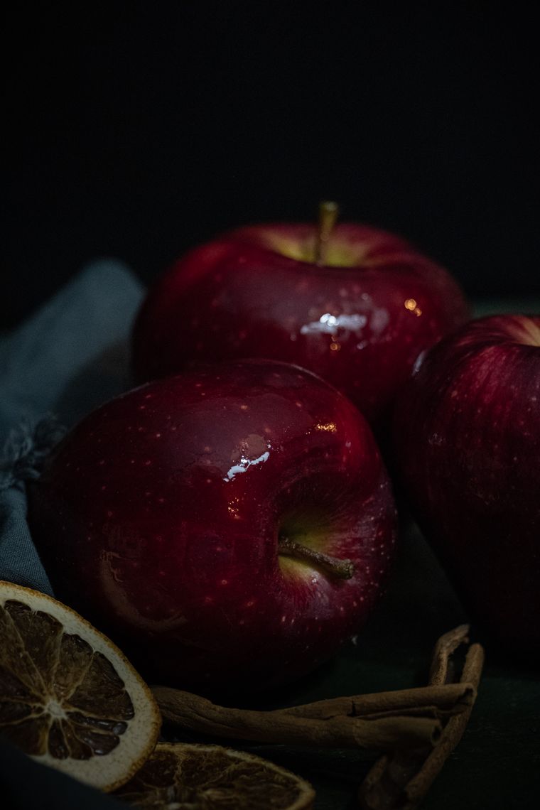 Dark, moody still life of red apples with cinnamon sticks and dried orange slices — photo by Merve on Pexels