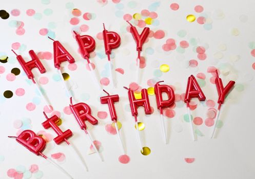 Festive birthday candles spelling 'Happy Birthday' surrounded by colorful confetti.
