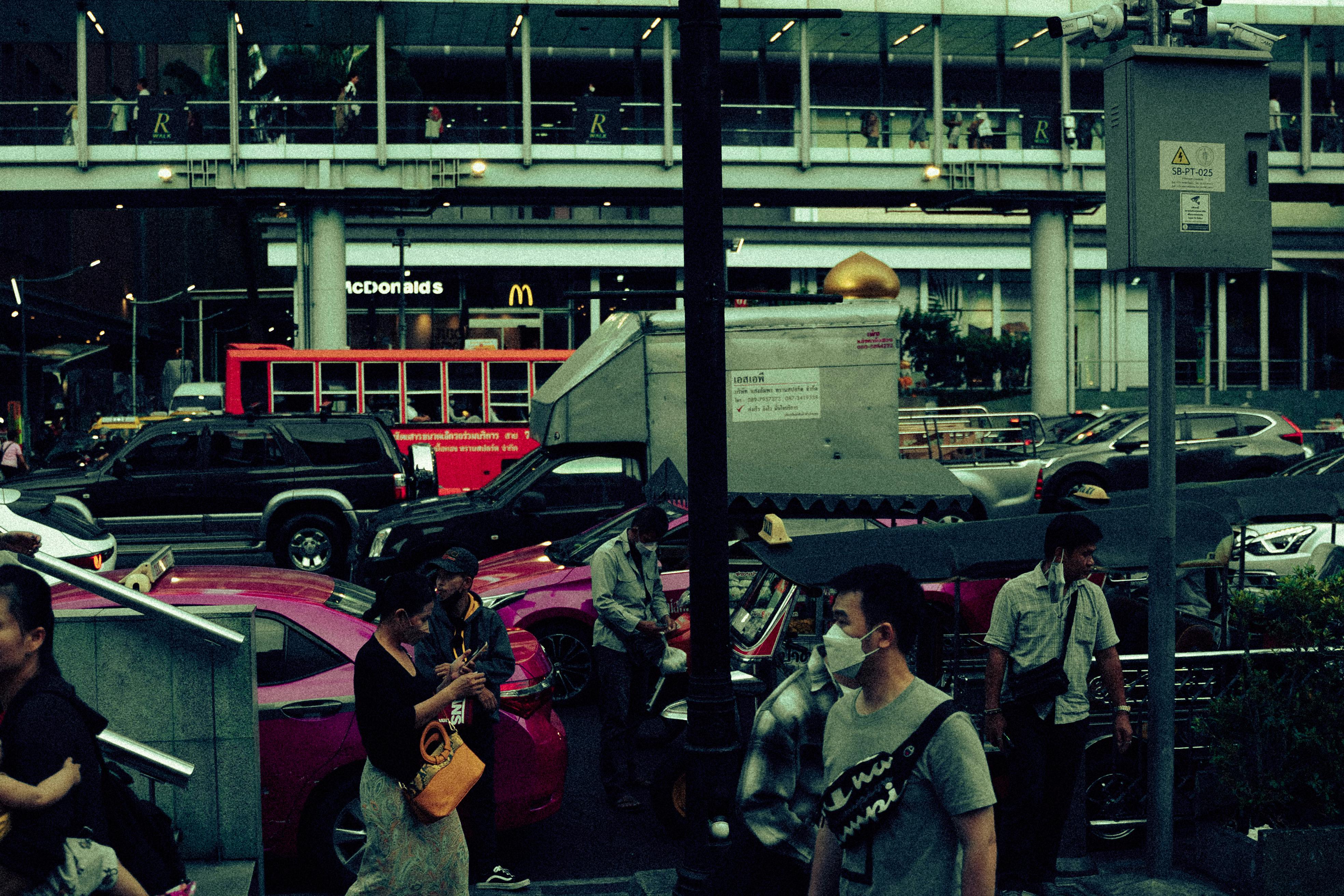 Busy Bangkok street with traffic and pedestrians near McDonald's at dusk.