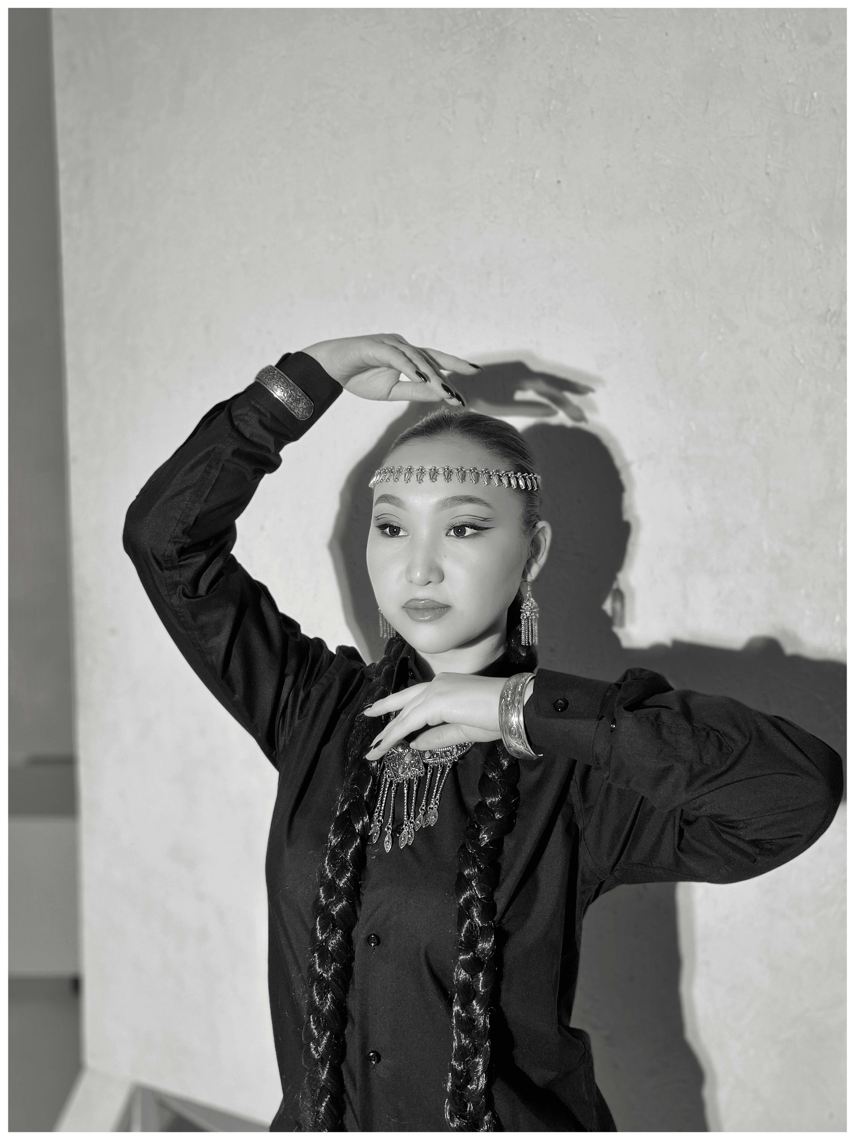 Black and white portrait of a woman in traditional attire posing gracefully against a textured wall.