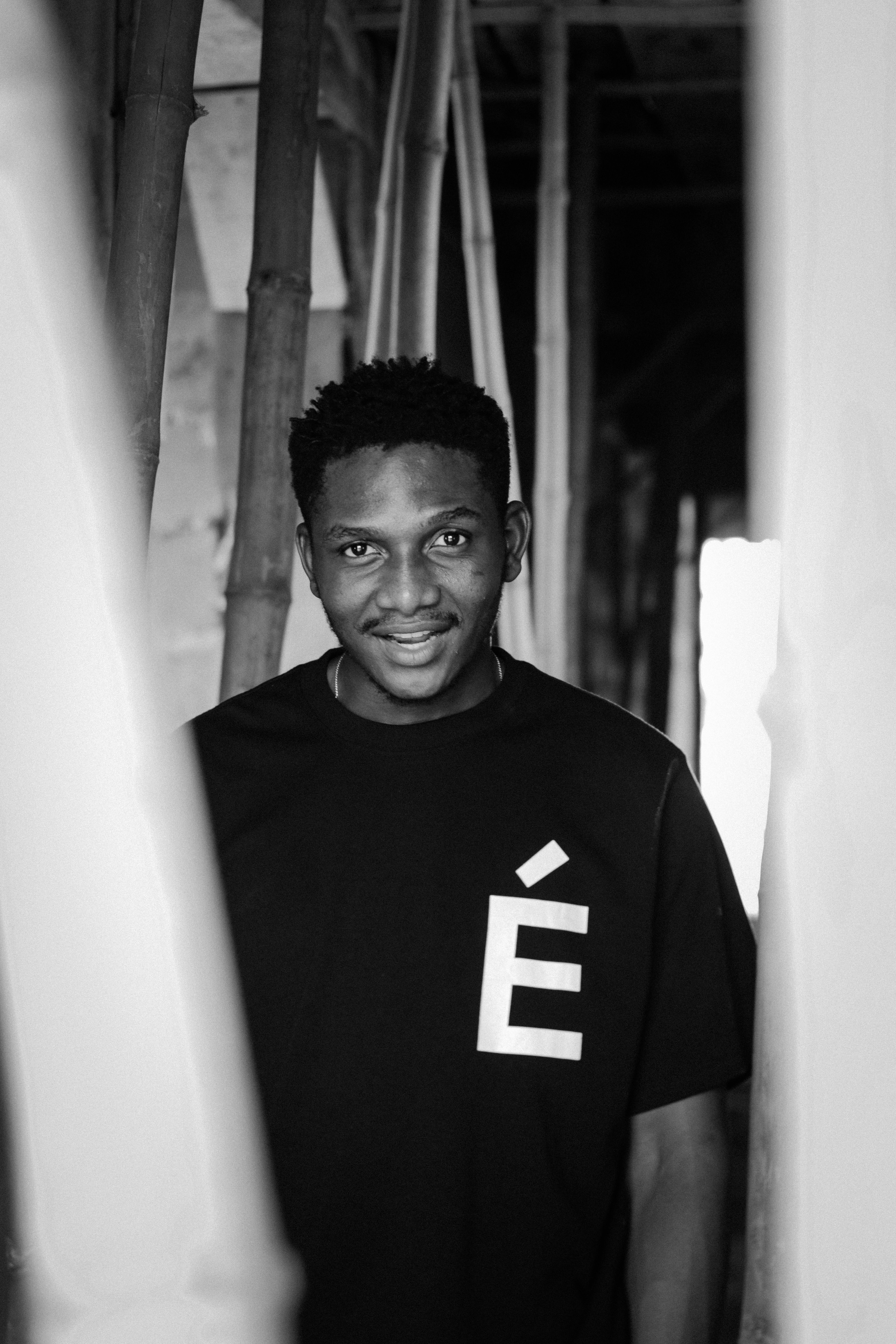 Artistic black and white portrait of a young man with short hair smiling in a stylish t-shirt indoors.