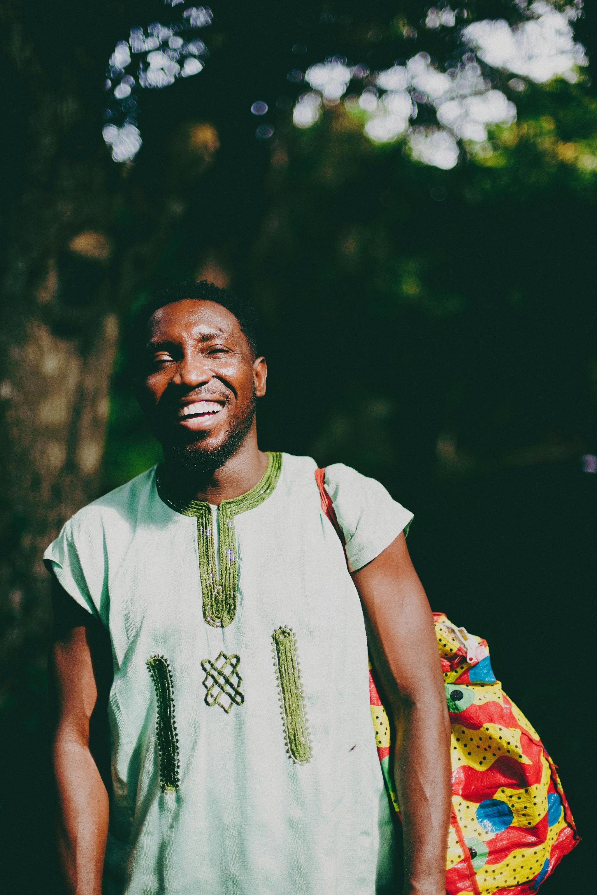 Smiling African man wearing traditional Nigerian attire outdoors with colorful backbag in Lagos, Nigeria.