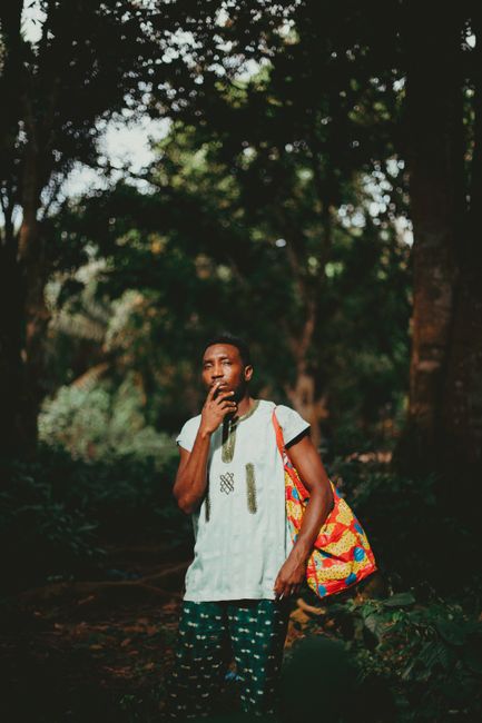 Man standing with a colorful bag under trees in Lagos, Nigeria. Fashion and nature blend.