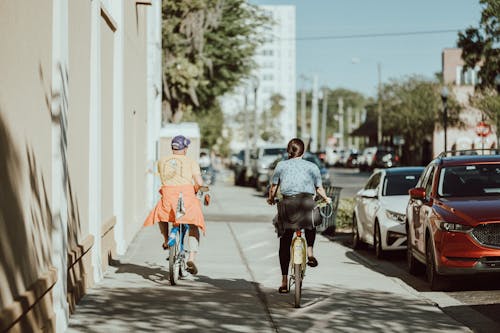 Two people riding bikes down a sidewalk