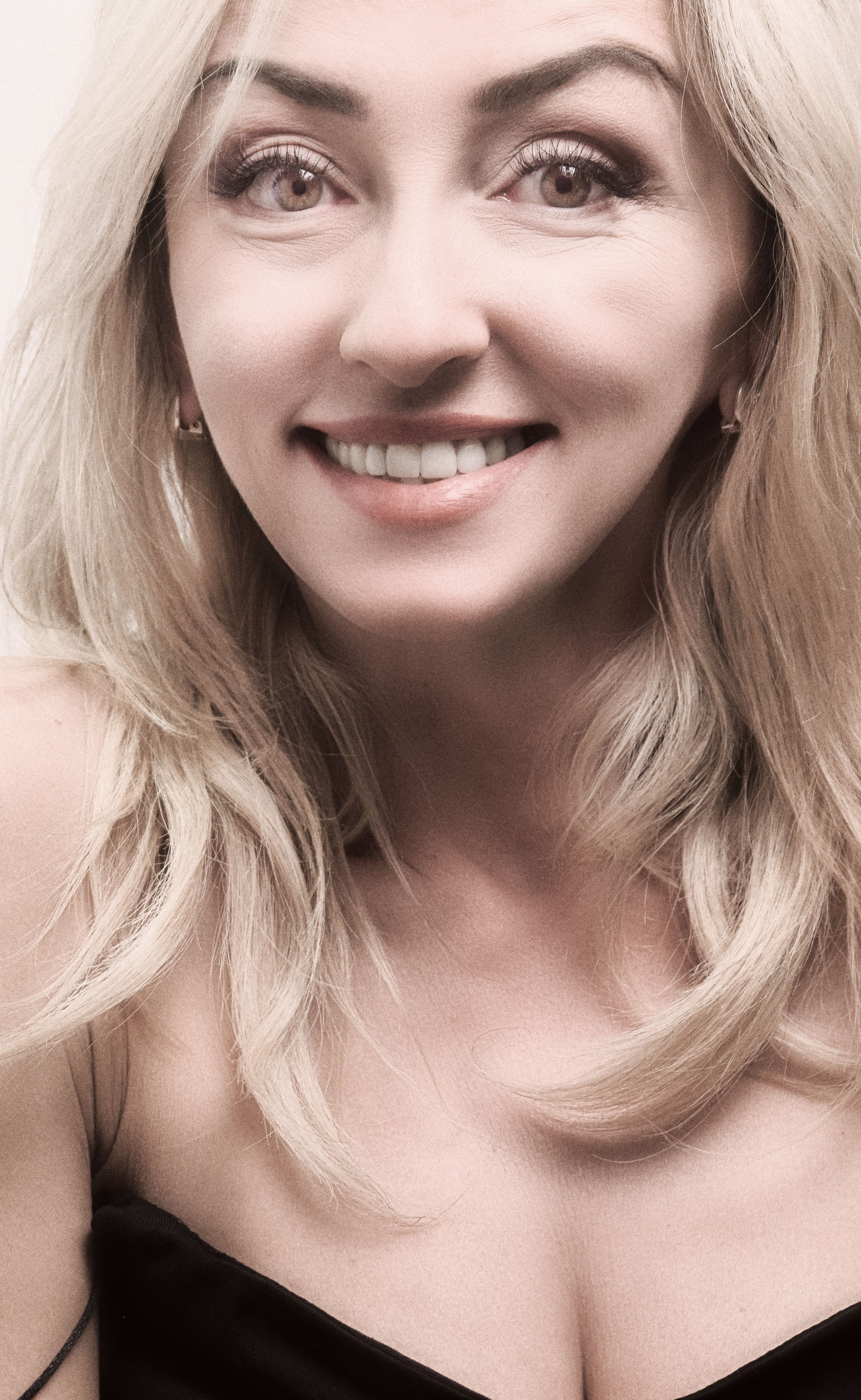 Elegant portrait of a blonde woman smiling with long hair and bright eyes.