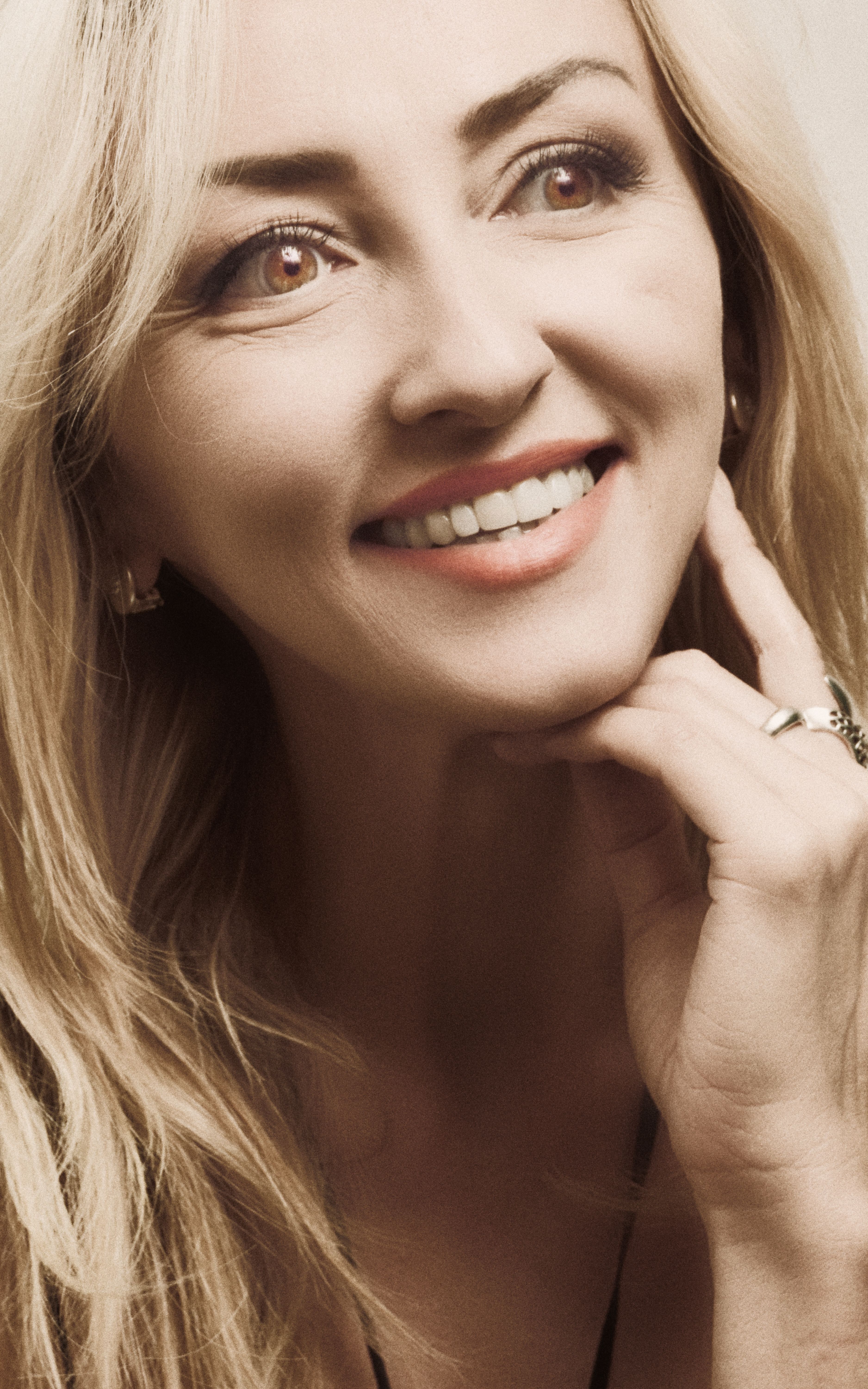 Close-up portrait of a smiling woman with hand on chin, exuding happiness.