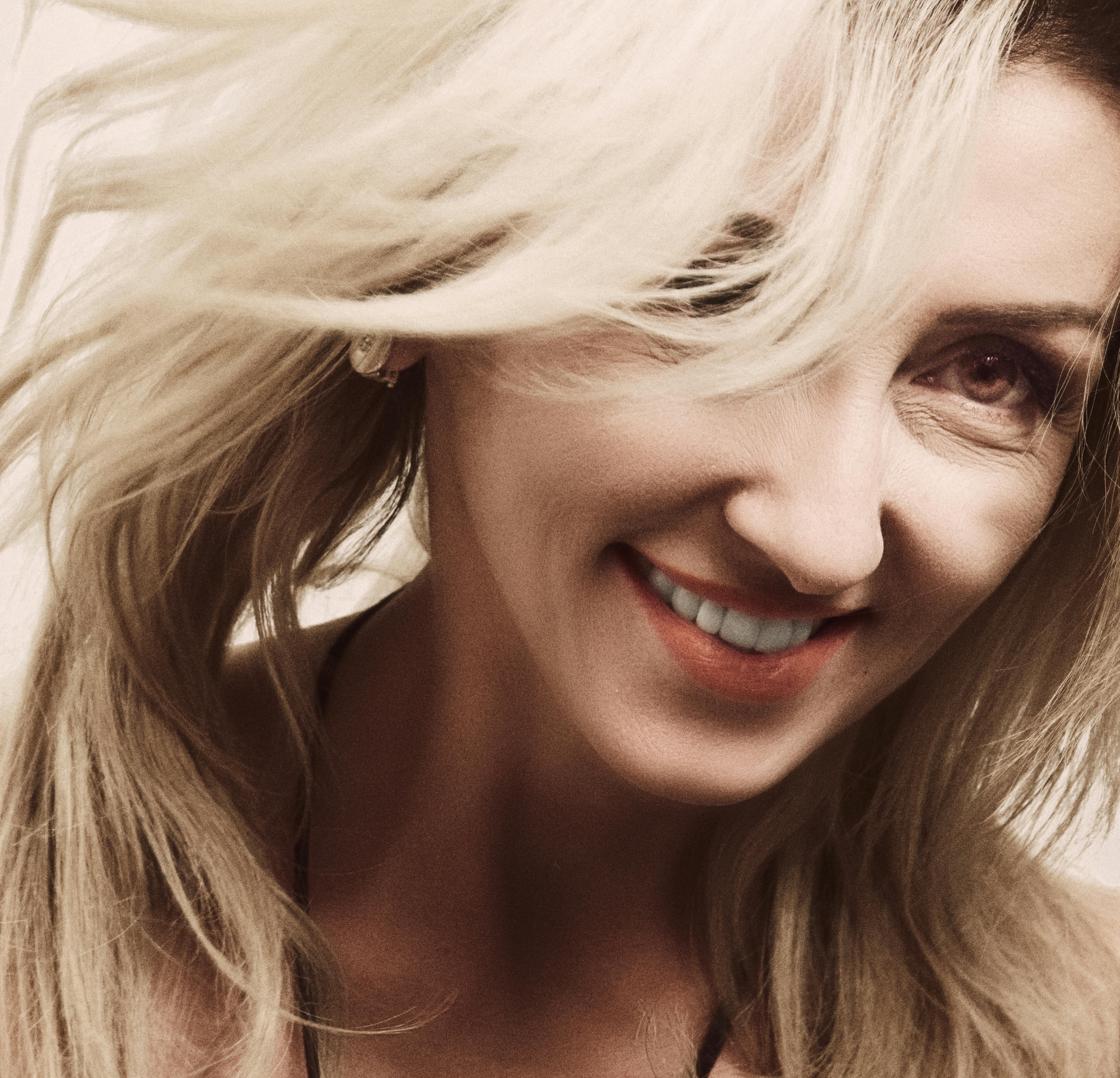 Close-up portrait of a smiling blonde woman with flowing hair.