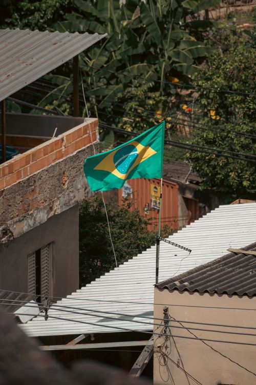 Free A Brazilian flag waves amongst rooftops in a residential urban area, showcasing vibrant patriotism. Stock Photo