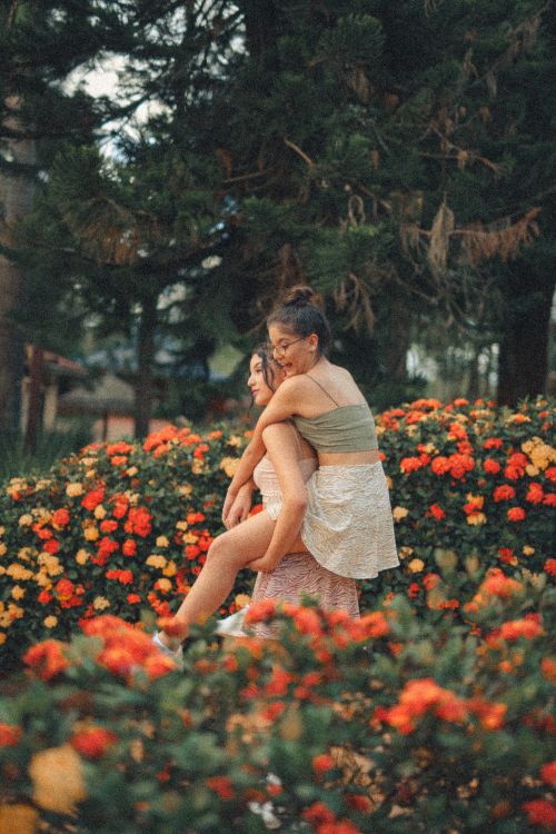 Free Two women share a joyful moment among vibrant flowers and lush greenery. Stock Photo