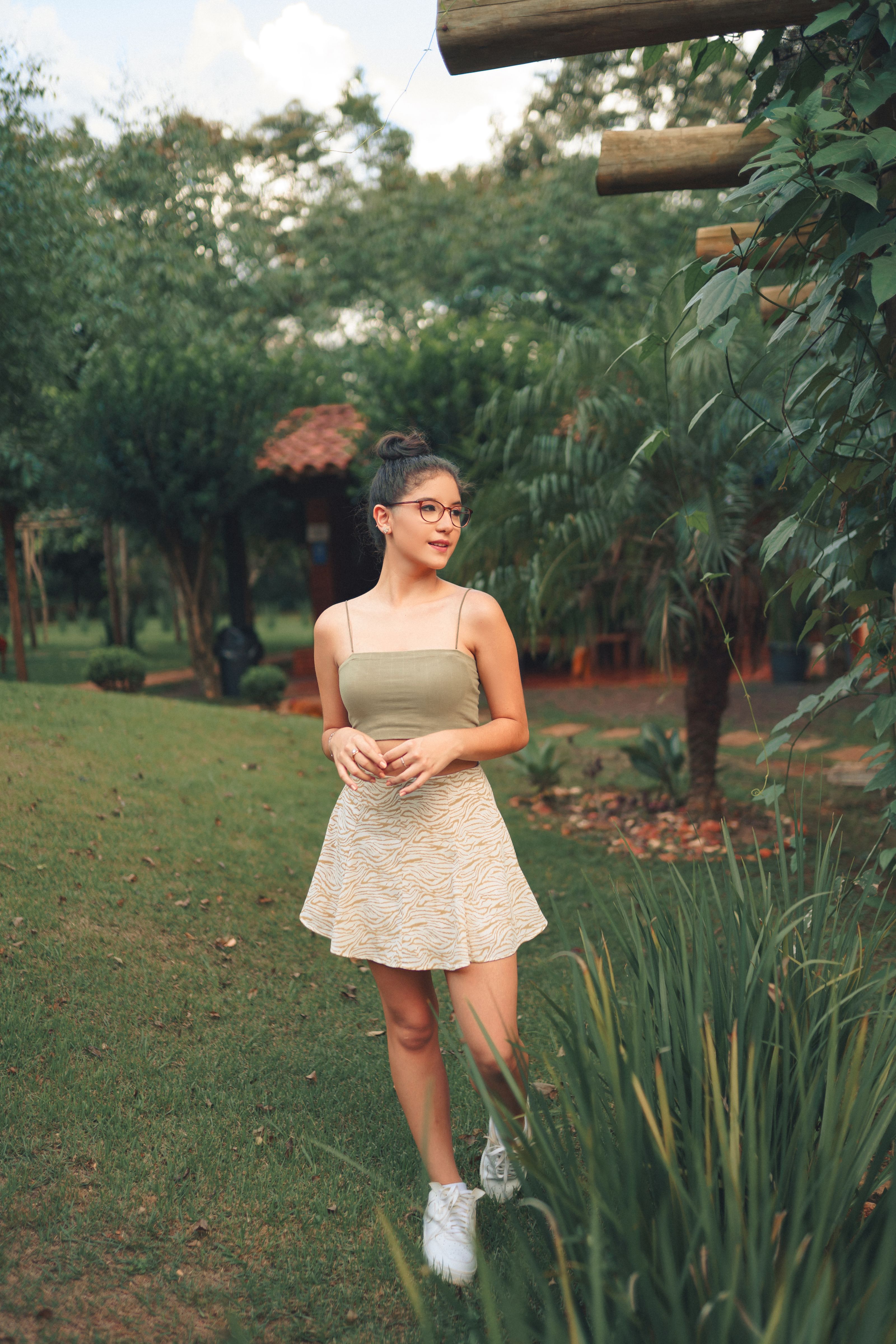 Mulher estilosa usando uma saia posa entre a vegetação exuberante, destacando as tendências da moda de verão.