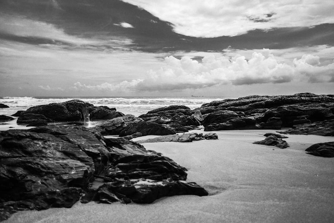 Grayscale Photography of Rocks on Seashore during Daytime