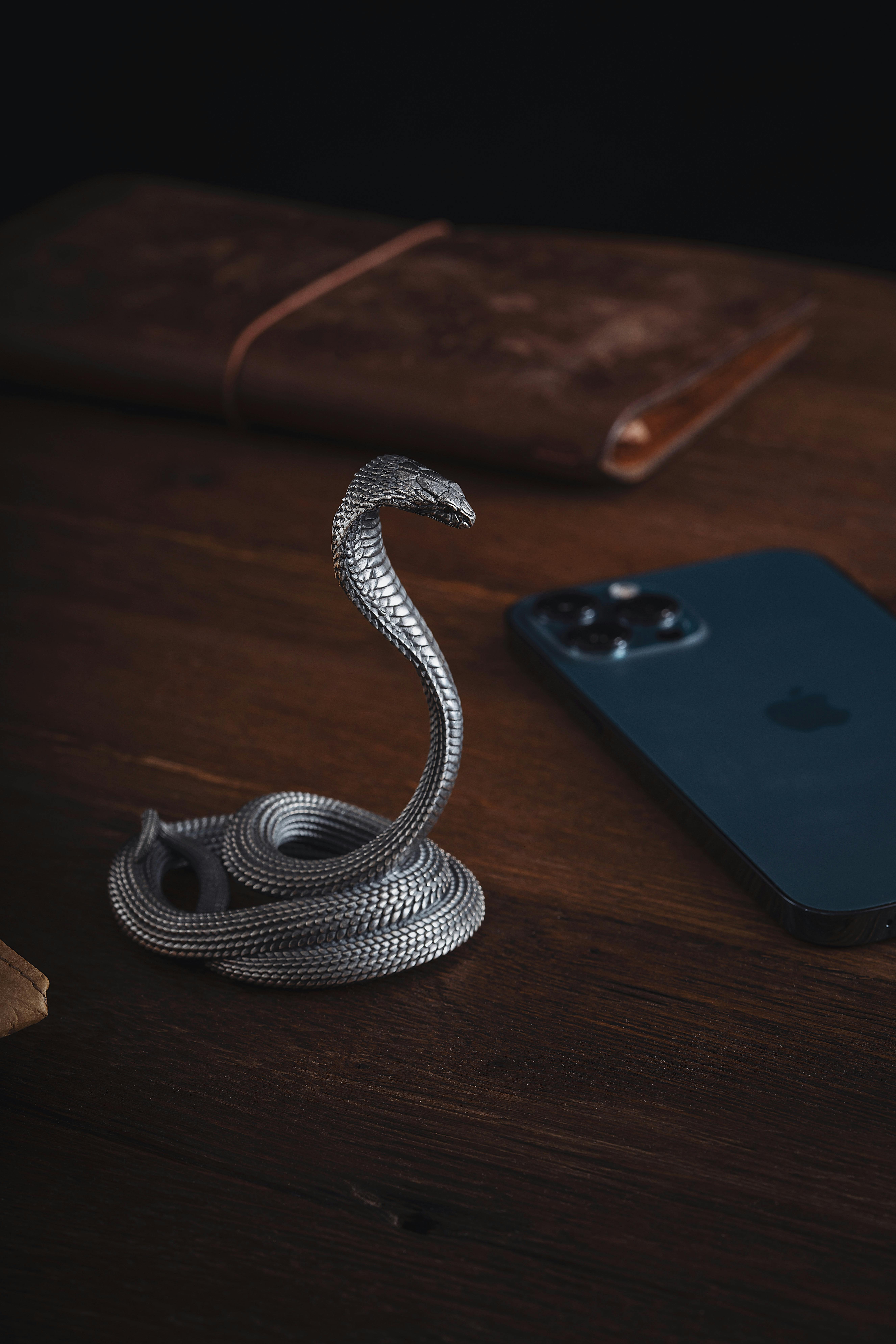 Elegant oxidized silver snake-shaped phone stand next to a smartphone on a wooden surface.