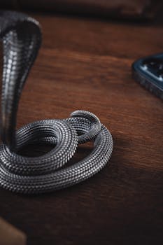 Handmade oxidized silver snake figurine used as a phone stand on wooden surface.