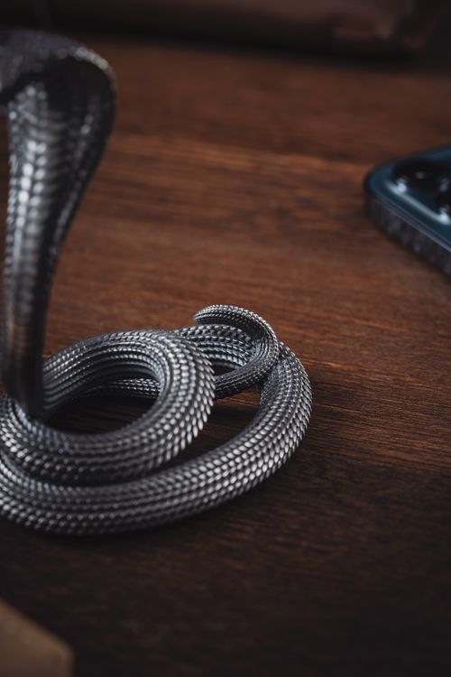 Free Handmade oxidized silver snake figurine used as a phone stand on wooden surface. Stock Photo