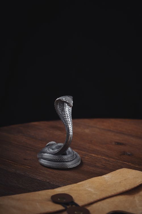 Free Close-up of an intricate cobra figurine on a wooden desk with a dark background. Stock Photo