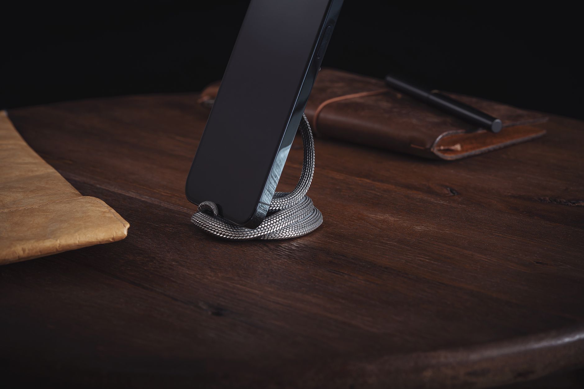 A sleek smartphone propped up by a snake figurine on a wooden desk. Sophisticated and modern.