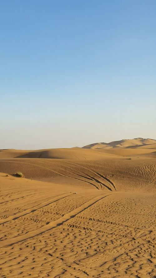 Free Discover the vast and serene Dubai desert dunes with tire tracks under a clear blue sky. Stock Photo