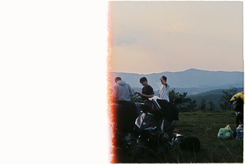 Free A group of friends standing by scooters on a grassy hill during sunset. Stock Photo