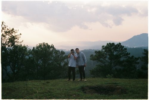 Free Two young men standing in a picturesque outdoor mountain setting with trees and clouds. Stock Photo