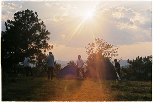 Free A serene camping scene with tents and people at sunset amidst trees and mountains. Stock Photo