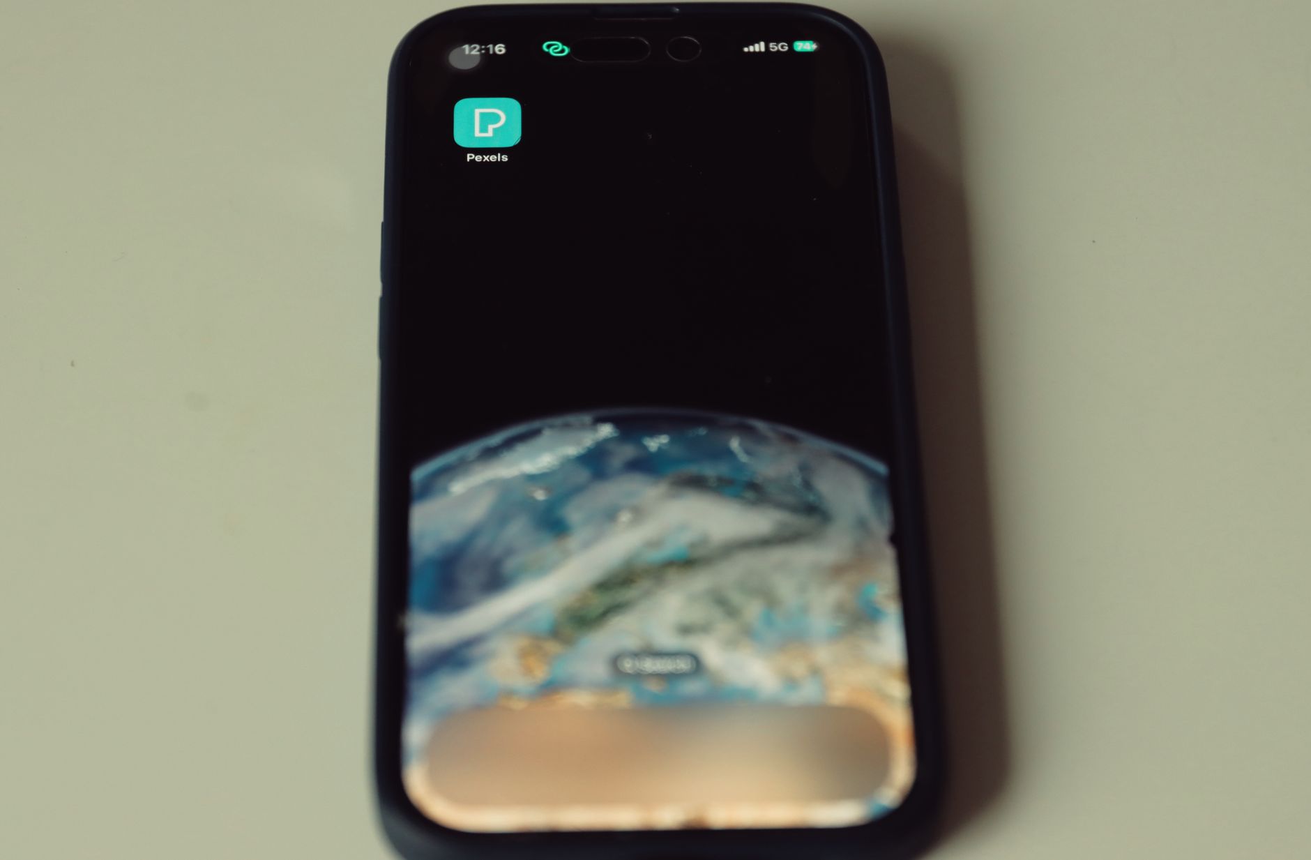 Close-up of smartphone showing Earth wallpaper and Pexels app icon on screen.