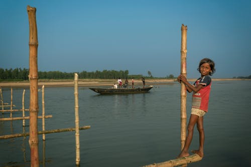 Child Standing and Holding Bamboo Poles over Water