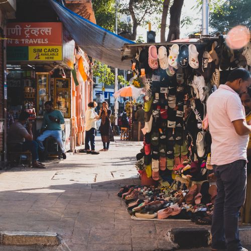 Free Colorful shoe stall in a bustling Mumbai street market with people shopping on a sunny day. Stock Photo