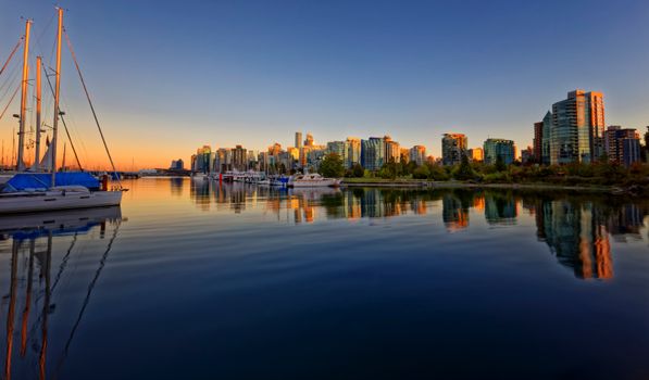 Stunning view of Vancouver skyline with boats reflecting on calm water at sunset.