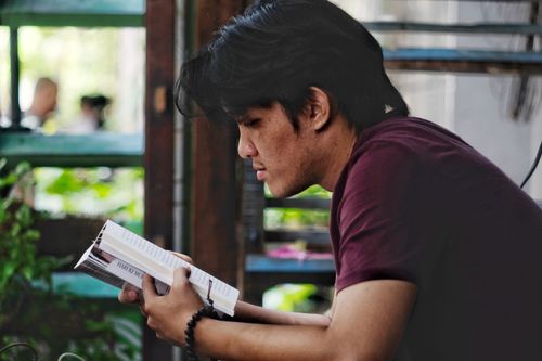 Free A young man intently reading a book indoors, captured in a relaxed and leisure setting. Stock Photo