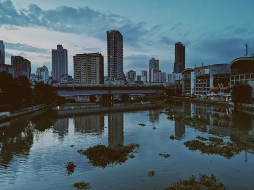 Free A picturesque view of a city's waterfront skyline reflecting in the river at twilight, showcasing urban architecture. Stock Photo